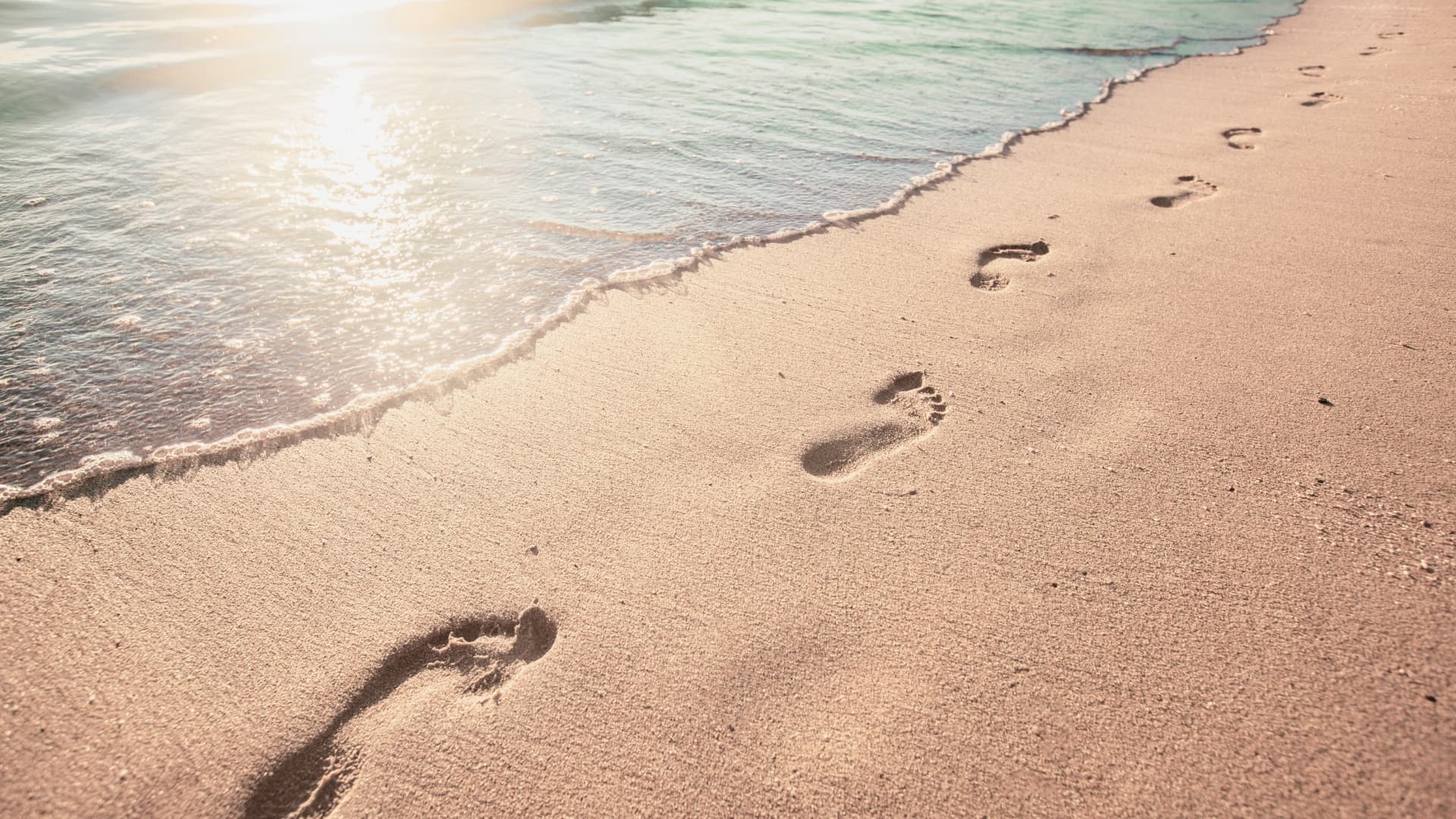 Lábnyomok a homokban a tengerparton, amelyek egy irányba vezetnek